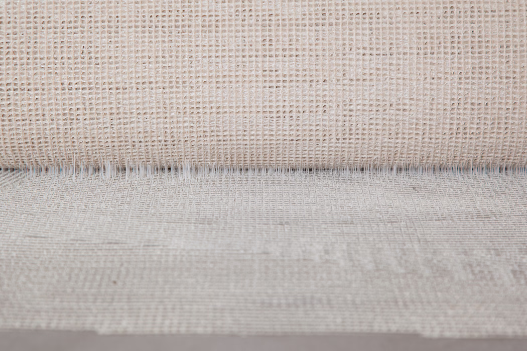 UZIN_Application Image_UZ57_2_6268_2018-11 Close-up of a neutral beige woven fabric with an open, grid-like weave. The top shows a rolled edge creating a fine shadow line, while irregular threads and natural fiber variations give a tactile, rustic appearance. Soft, even lighting highlights the texture and subtle depth.